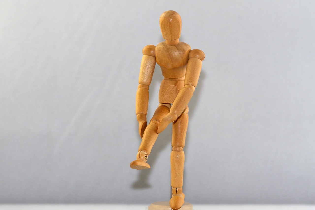 A wooden figurine showing pain in the leg.